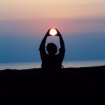 silhouette of person with both hands over his head tracing the sun during golden hour photography