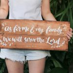 a woman holding a wooden sign that says as for me and my family we will