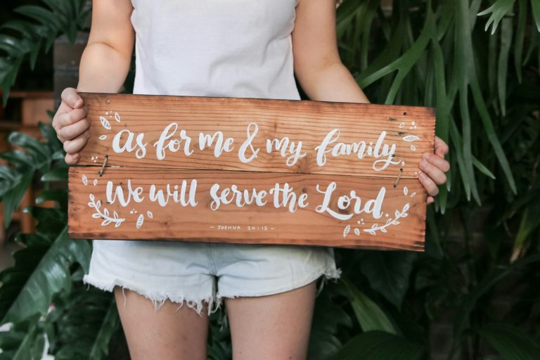 a woman holding a wooden sign that says as for me and my family we will